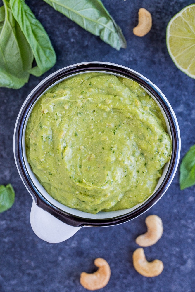 Avocado Pesto Sauce Recipe in a bowl with ingredients scattered around it