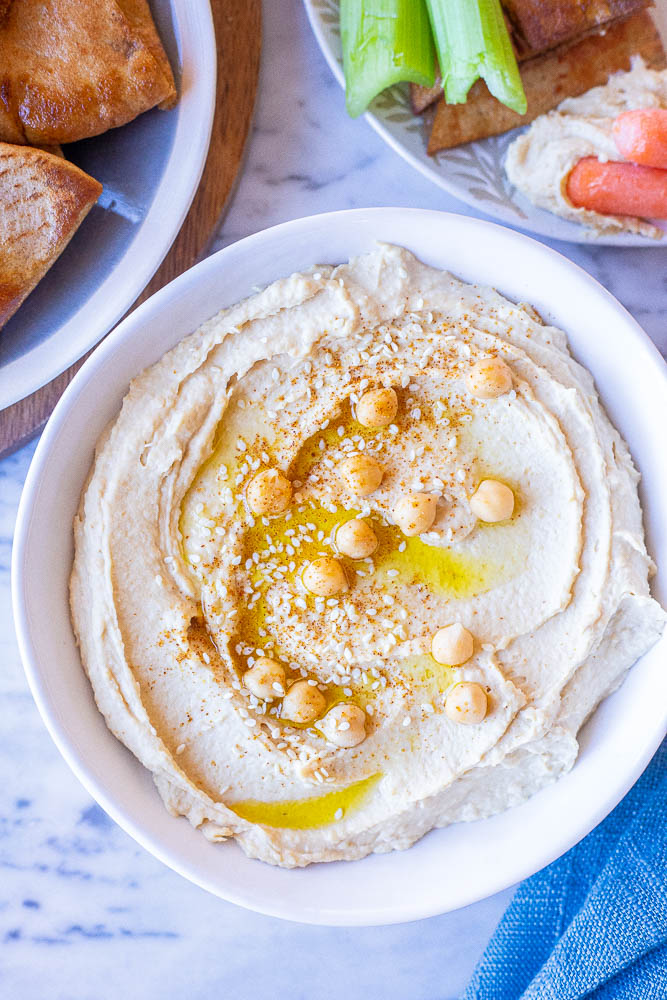 A bowl of the creamiest hummus recipe with pita bread and veggies