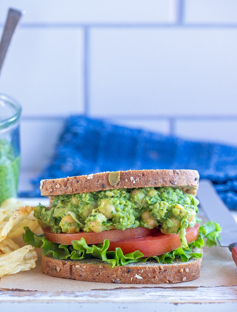 avocado pesto chickpea sandwich with potato chips on a cutting board