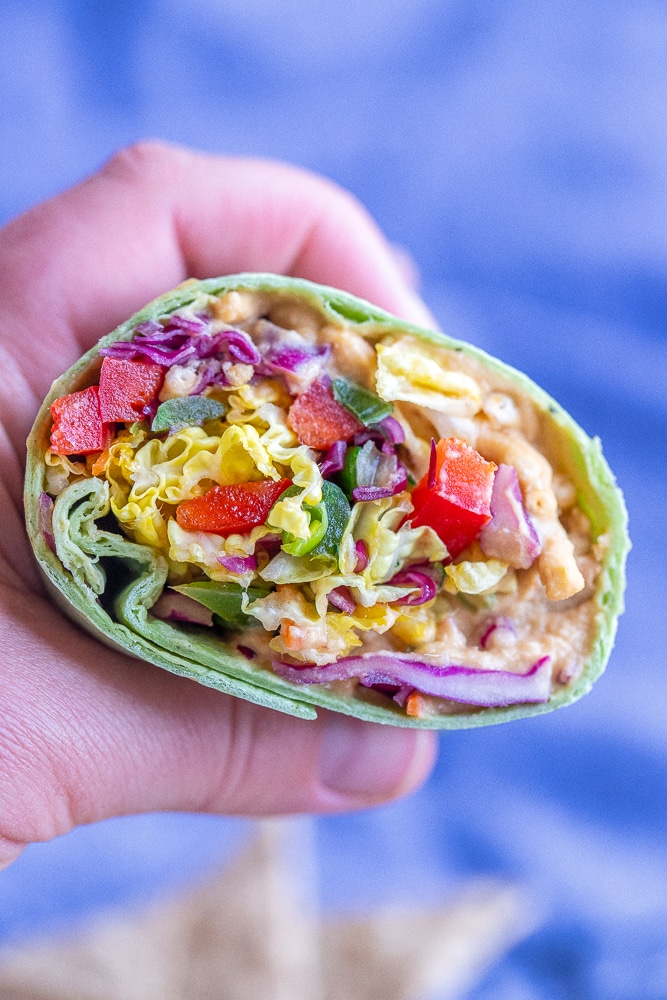 a hand holding a rainbow veggie hummus wrap