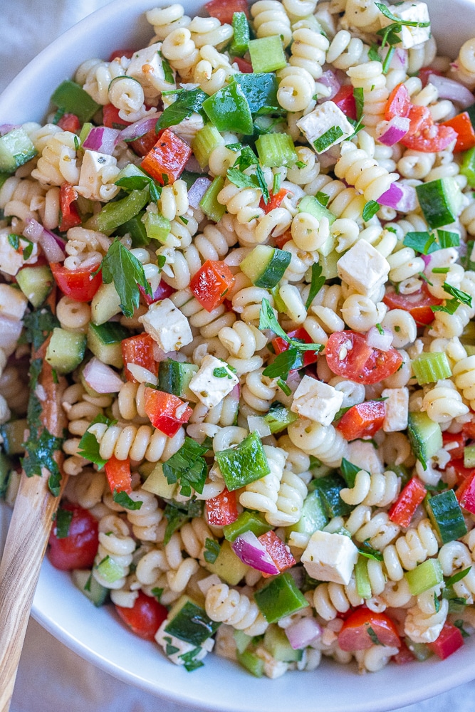 close up of easy vegetarian pasta salad in a bowl with a wooden spoon