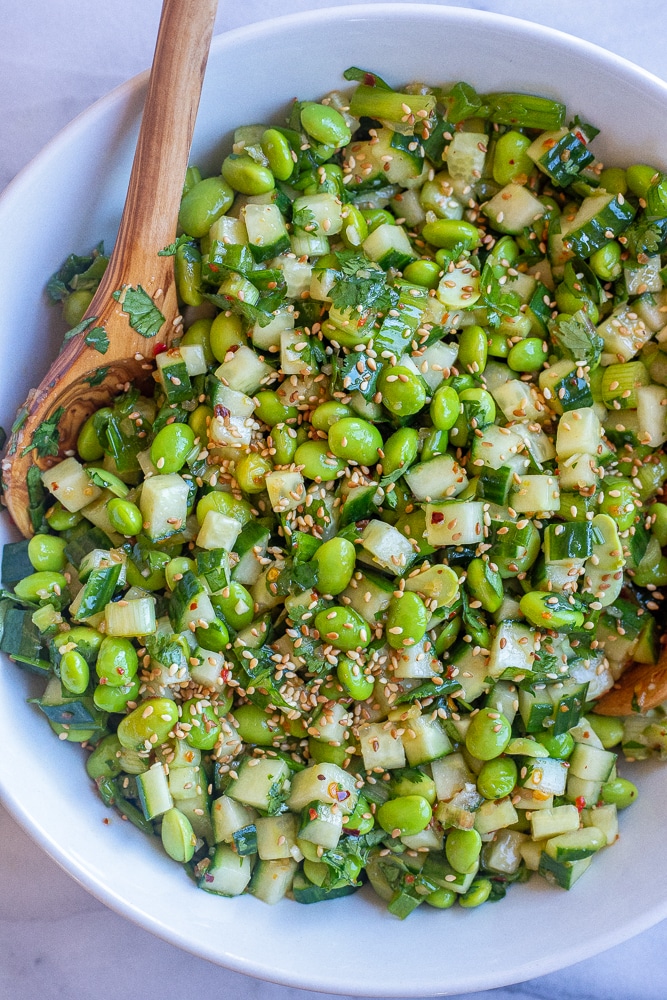 close up of a bowl of cucumber edamame salad with wooden spoons