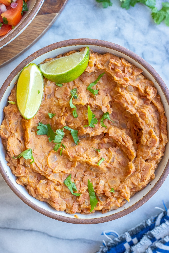 bowl of homemade refried beans topped with cilantro and limes
