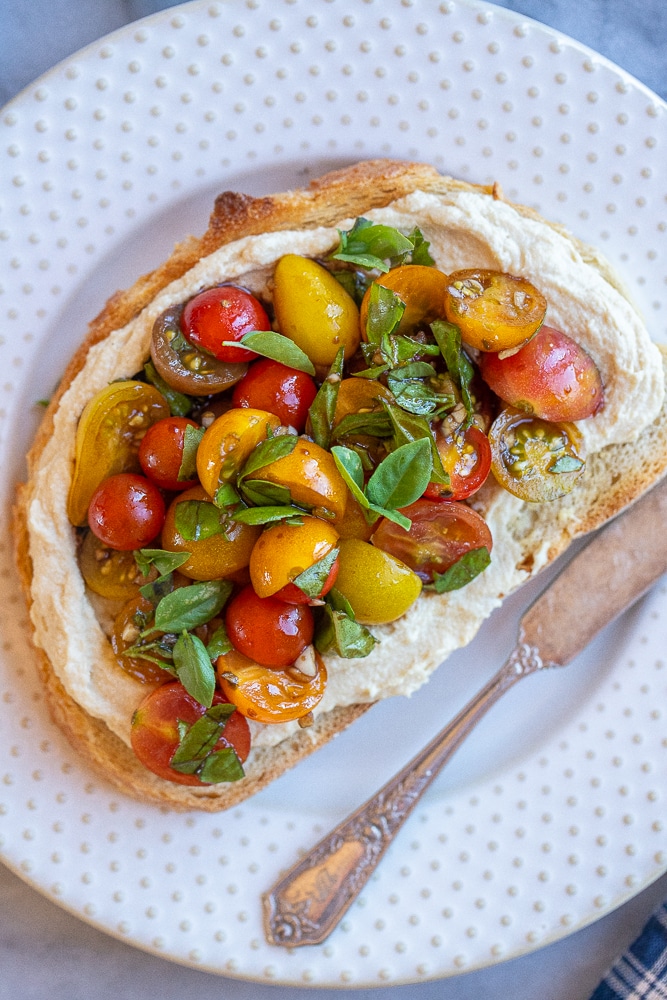 close up of hummus toast with bruschetta on a plate