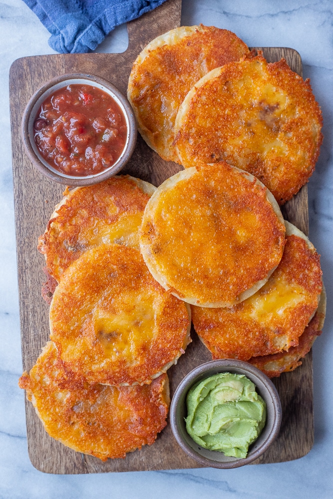 cutting board topped with mini cheese crisps and salsa and guacamole