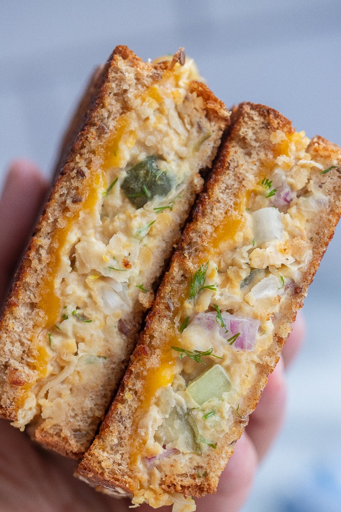 a hand holding two tuna chickpea salad melts