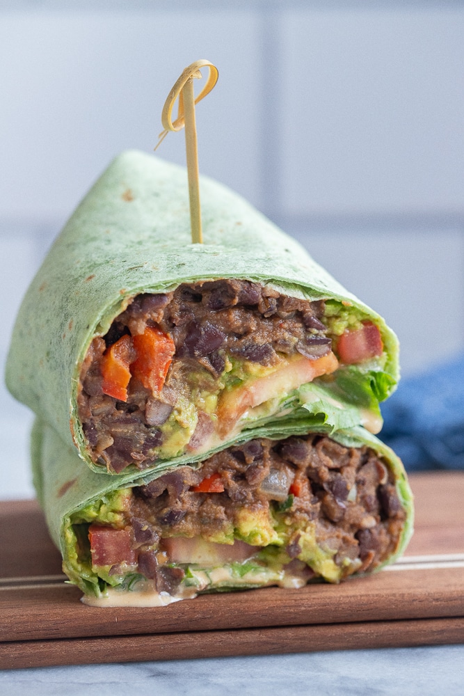 a vegan black bean wrap sliced in half on a cutting board
