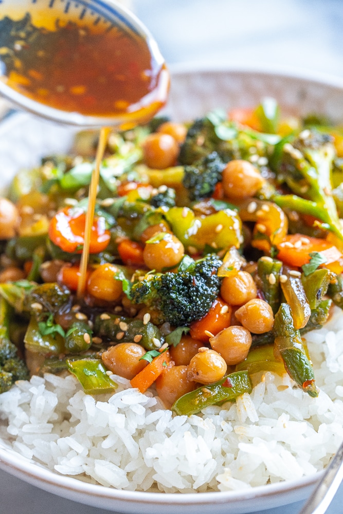 a spoon pouring sauce over a bowl of stir fry vegetables