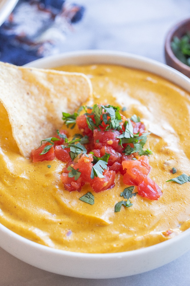close up of a chip being dipped into a bowl of vegan cheese sauce