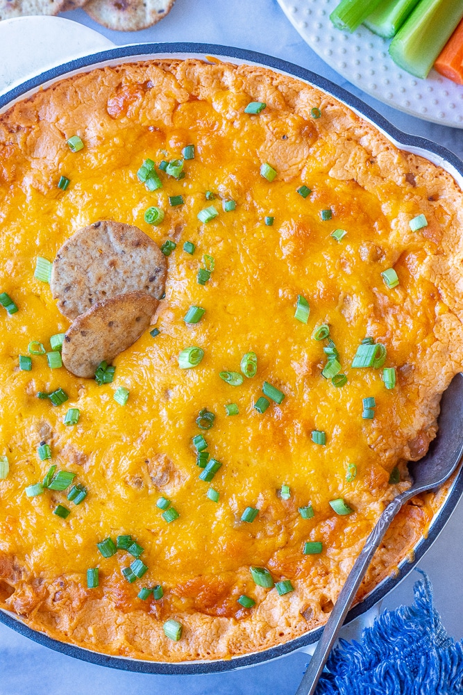 a skillet full of vegetarian buffalo chickpea dip with green onions and crackers