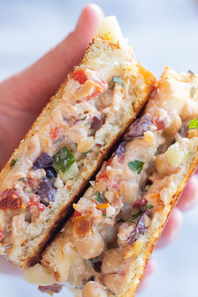 A hand holding a sliced open greek chickpea salad melt