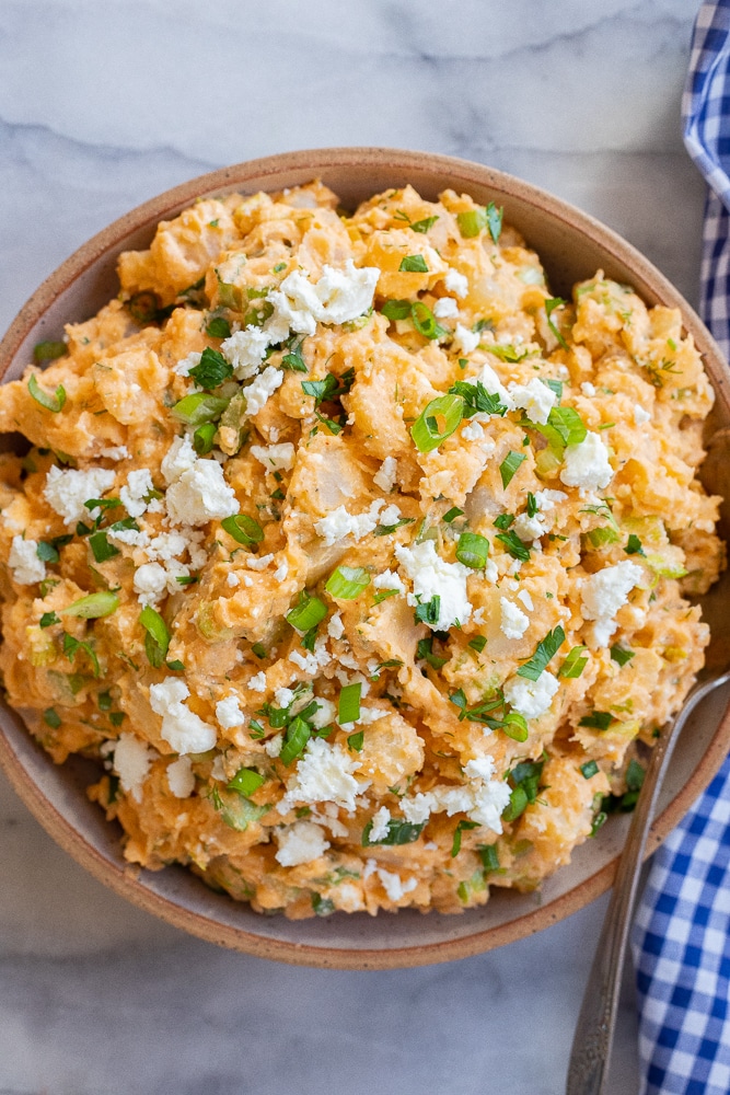 bowl of buffalo potato salad topped with feta cheese and green onion