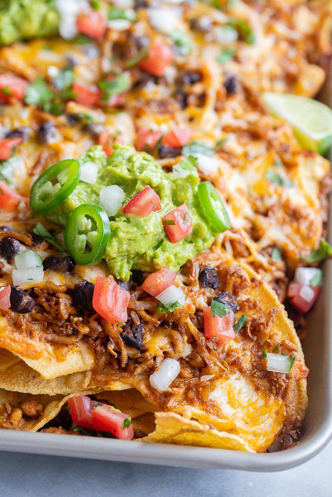 close up of a pan of shredded tofu nachos topped with guacamole