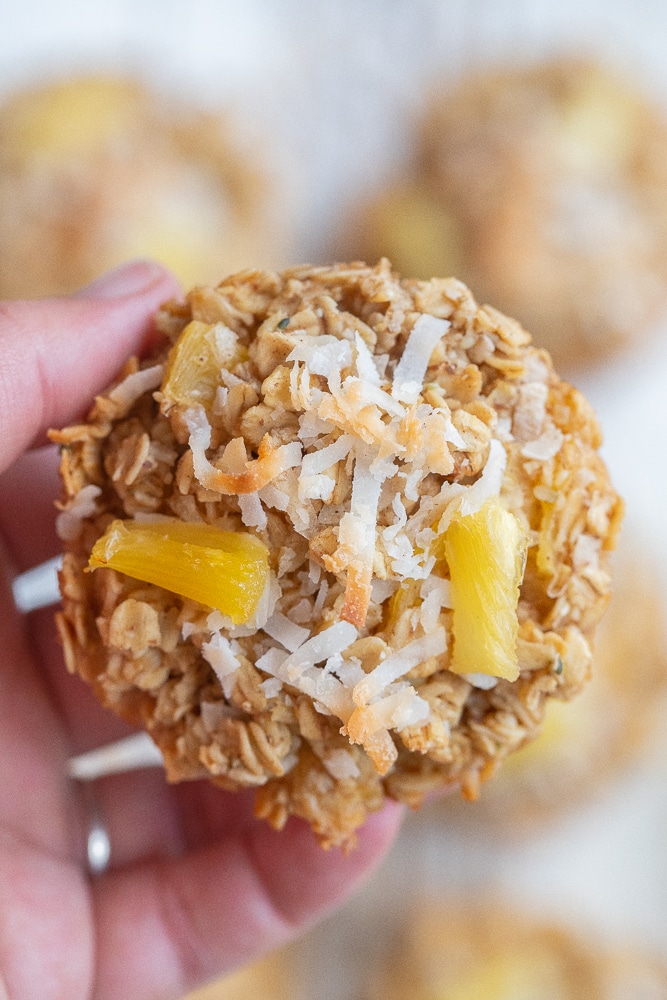 a hand holding a Pina Colada Baked Oatmeal Cup topped with pineapple and coconut
