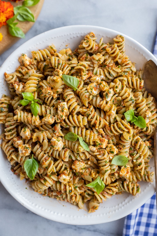 white dinner bowl full of kale and sun-dried tomato pasta with feta cheese