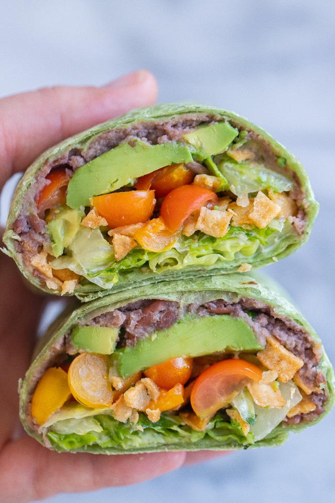 close up of a black bean wrap cut in half being held by a hand
