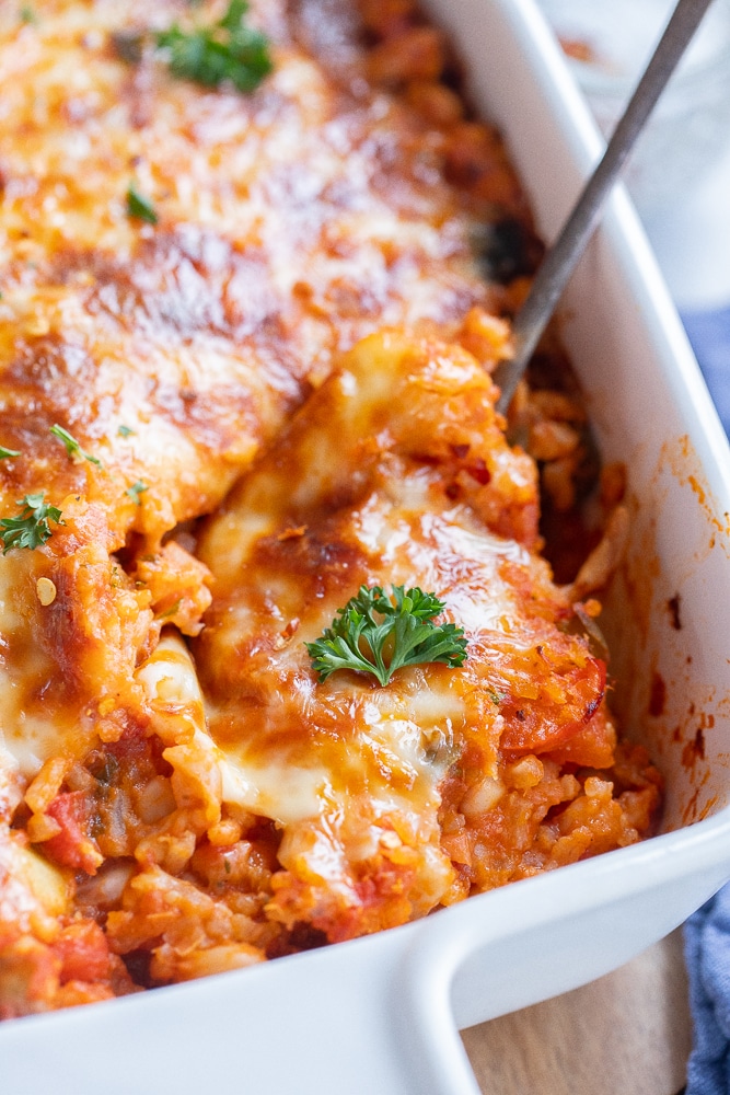 close up of a pan of vegetarian pizza casserole with a serving spoon