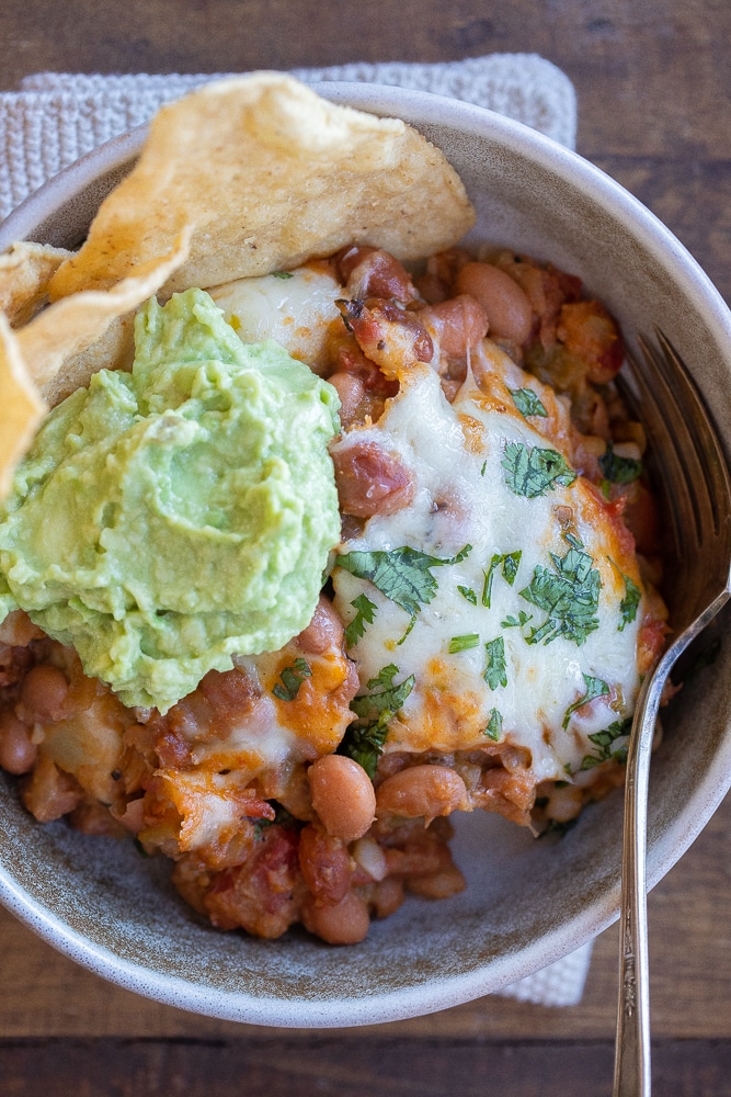 cheesy green chile pinto beans in a bowl with guacamole and tortilla chips