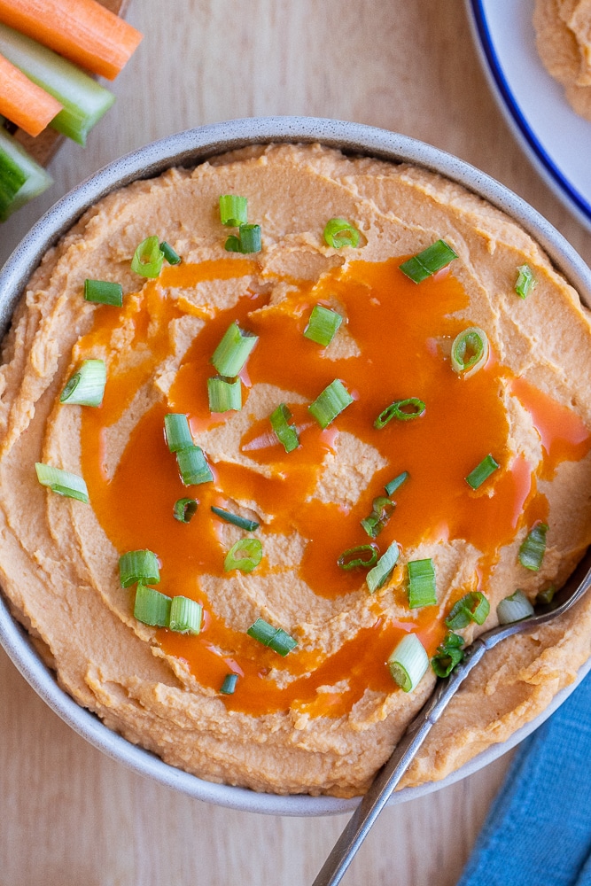 Bowl of creamy buffalo hummus served with carrots and celery