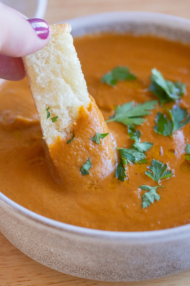 close up of a hand dipping garlic bread into this roasted ratatouille soup
