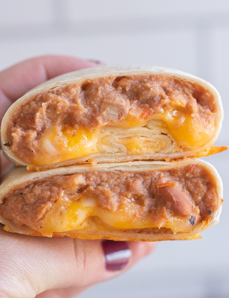 close up of a hand holding a bean and cheese burrito that has been cut in half