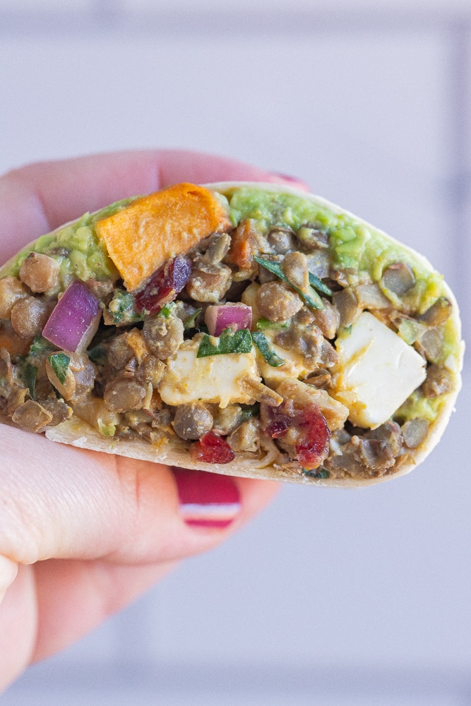 close up of a hand holding a curry lentil wrap with roasted sweet potatoes