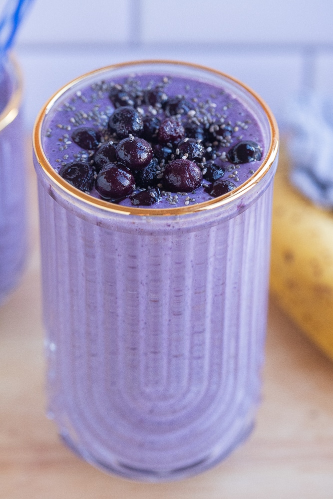 close up of a glass of blueberry banana smoothie topped with blueberries and chia seeds