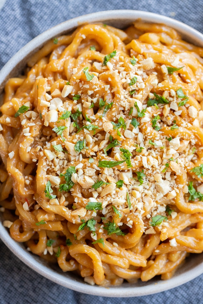 close up of a bowl of vegan peanut noodles topped with chopped peanuts and cilantro
