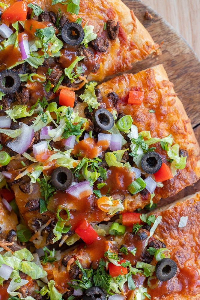 close up of a slice of vegetarian taco pizza topped with lettuce, tomato and onion
