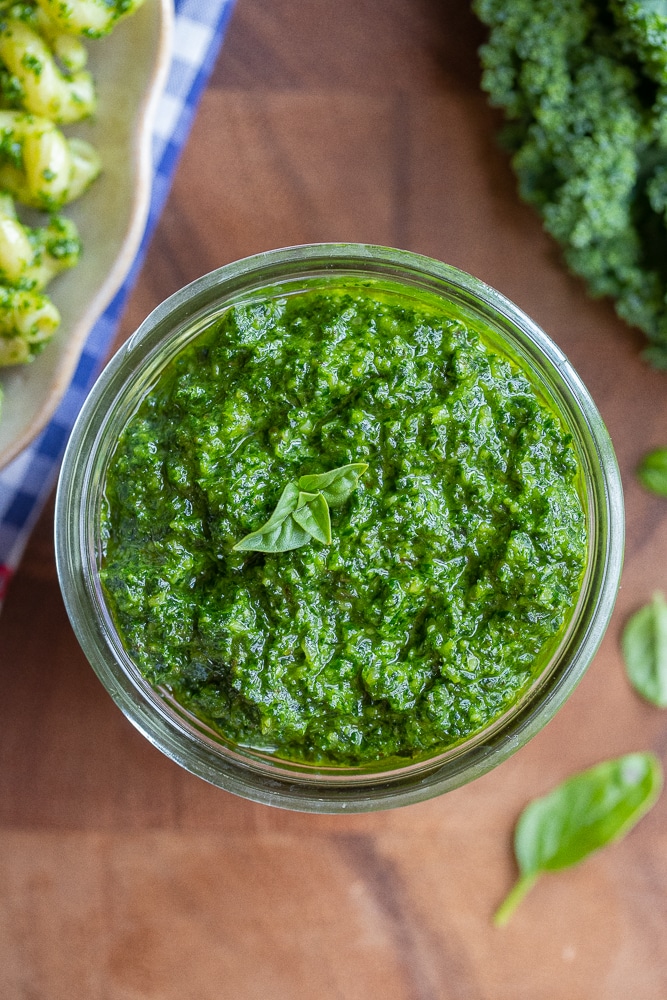 kale pesto sauce in a glass jar with pesto pasta on a plate