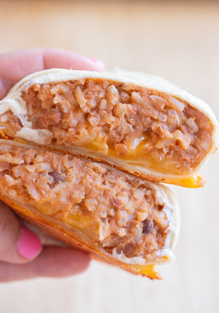 close up of a hand holding a cheesy bean and rice burrito that has been cut in half