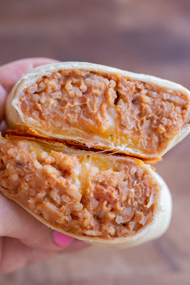 close up of a hand holding a bean burrito that has been cut in half