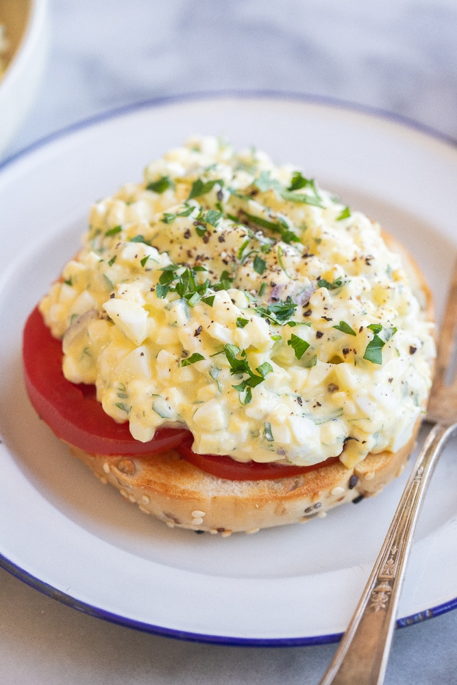 close up of a bagel topped with sliced tomato and a few spoonfuls of the cottage cheese egg salad
