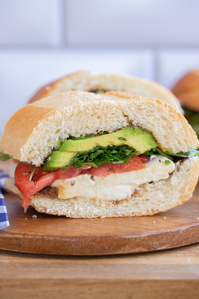 avocado caprese sandwich cut in half on a cutting board