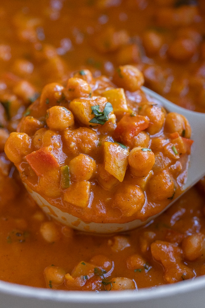 close up of a soup ladle full of pumpkin chickpea curry with vegetables