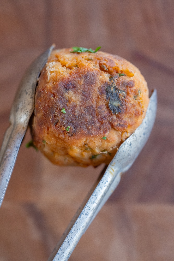 close up of a crispy browned vegetarian meatball being held by a tong