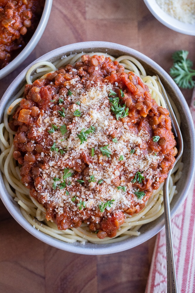 spaghetti with meaty lentil sauce in a bowl with parmesan cheese and parsley