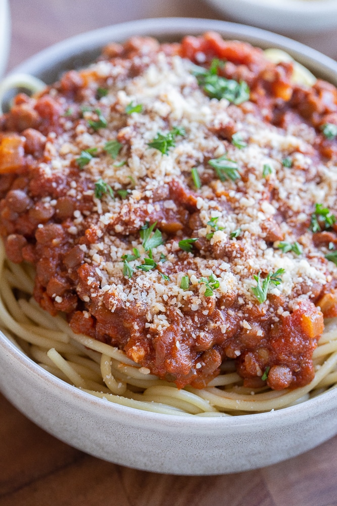 Close up of a bowl of meaty lentil spaghetti topped with parmesan