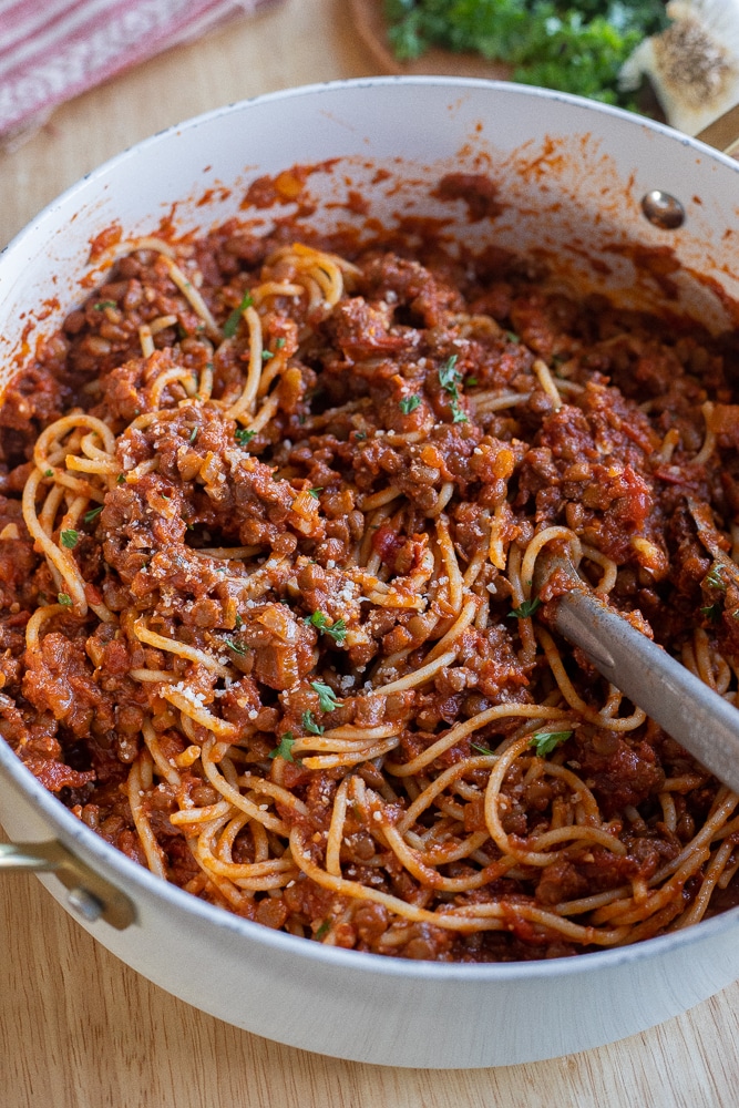 saucepan full of spaghetti with meaty lentil sauce topped with parmesan and fresh parsley