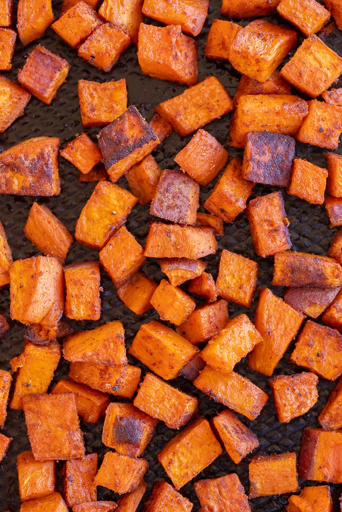 close up of seasoned roasted sweet potatoes on a sheet pan