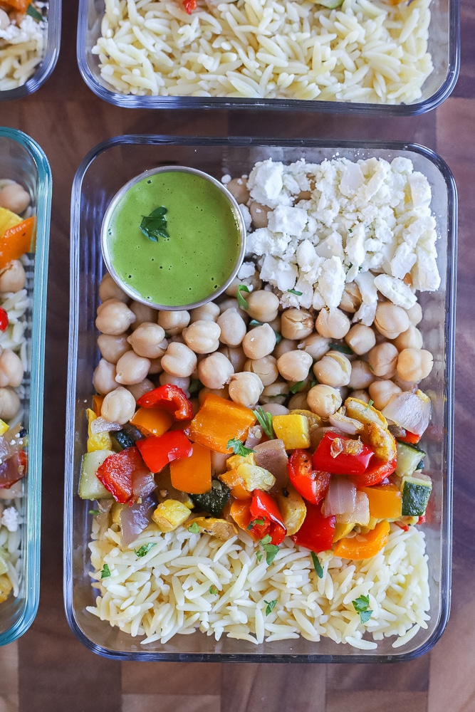 close up of a meal prep container filled with orzo, roasted vegetables, chickpeas and feta cheese