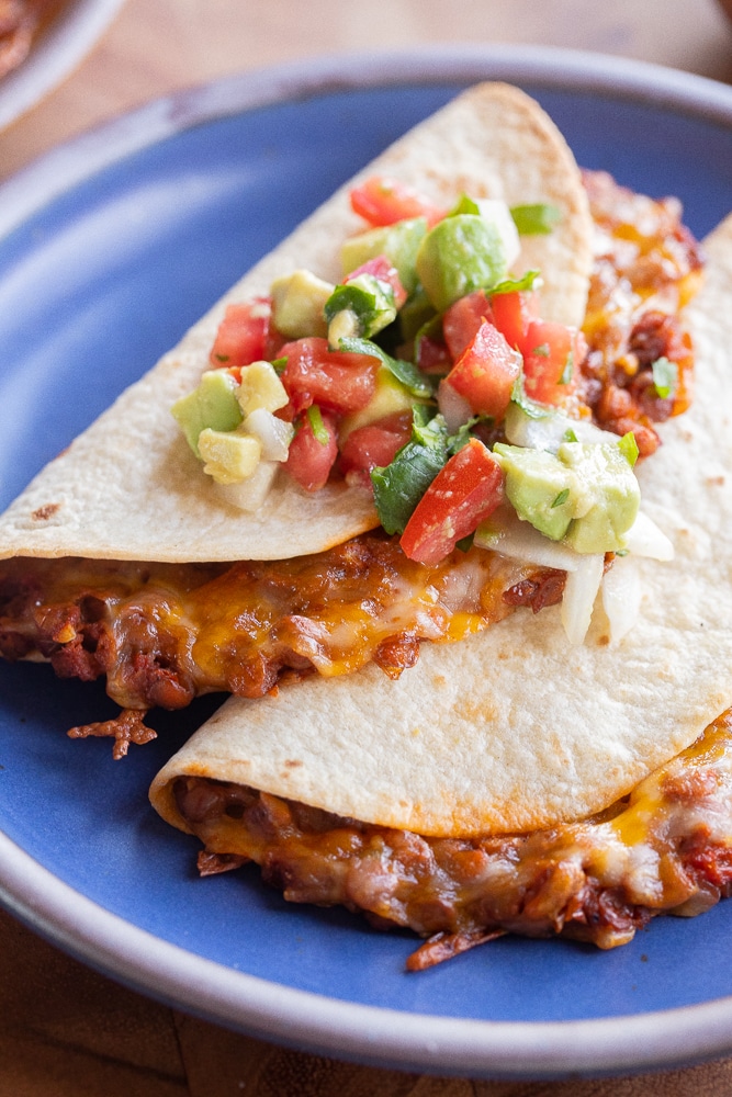 close up of a plate of two cheesy lentil tacos topped with tomato