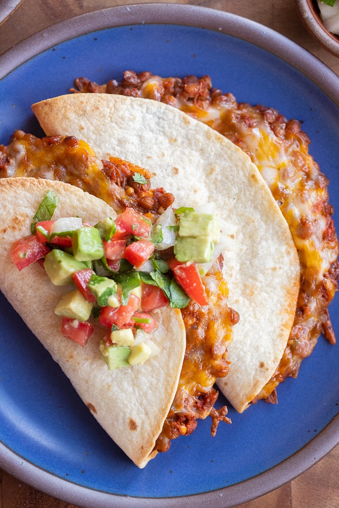 two lentil tacos on a blue plate topped with tomato and avocado